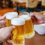 Three hands clinking frothy beer mugs
