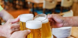 Three hands clinking frothy beer mugs