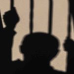 Shadow of a person gripping jail bars