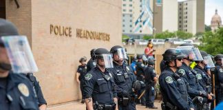 What REALLY Toppled POLICE CHIEF After Shootout? Police officers in riot gear stand in formation outside a headquarters building