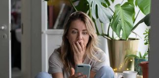 Woman sitting by plants looking at smartphone with surprised expression