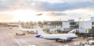 Airplanes at airport gates during sunset with ground vehicles and jet bridges