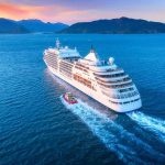 Cruise ship sailing at sunset near mountainous coastline