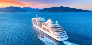 Cruise ship sailing at sunset near mountainous coastline