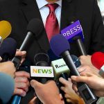 Press microphones surround a suited spokesperson