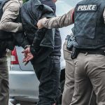 Police officers arresting a person beside a car
