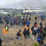 Large crowd of people walking through a field with small fires