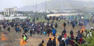 Large crowd of people walking through a field with small fires