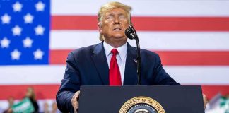 person speaking at a podium with U.S. flag backdrop