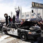 Damaged police car surrounded by protesters on a city street