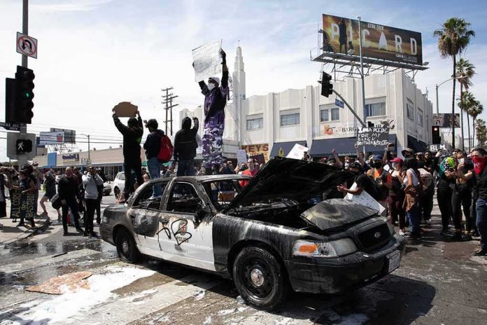 shutterstock_1745191118 Damaged police car surrounded by protesters on a city street