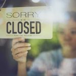 Person holding a closed sign on a shop window