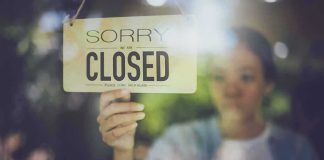 Person holding a closed sign on a shop window