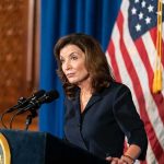 Woman at podium speaking with microphones and U.S. flag behind