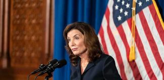 Woman at podium speaking with microphones and U.S. flag behind