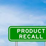 Green road sign reading product recall against blue sky