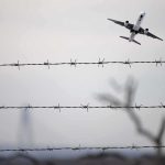 Airplane taking off above barbed wire fence