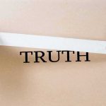 hands placing white tape over the word TRUTH on cardboard
