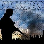 Silhouette of armed person by chain-link fence with barbed wire