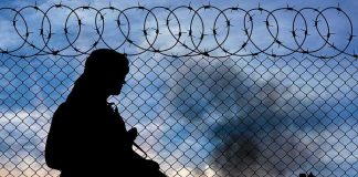 Silhouette of armed person by chain-link fence with barbed wire