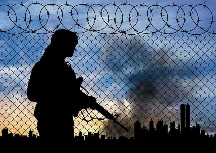 Silhouette of armed person by chain-link fence with barbed wire