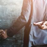 businessperson shakes hands while crossing fingers behind back
