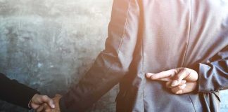 businessperson shakes hands while crossing fingers behind back