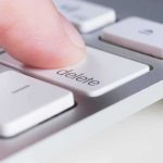 Finger pressing delete key on a white computer keyboard
