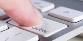Finger pressing delete key on a white computer keyboard
