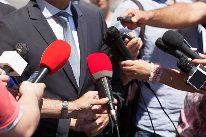 Person in suit surrounded by microphones during media interview