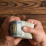 Hands holding a thick stack of U.S. hundred-dollar bills