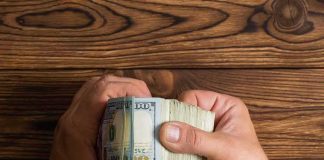 Hands holding a thick stack of U.S. hundred-dollar bills