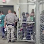 People standing inside chain-link holding area with an officer nearby