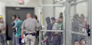 People standing inside chain-link holding area with an officer nearby
