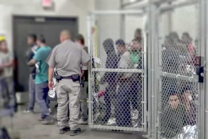 shutterstock_1229072188 People standing inside chain-link holding area with an officer nearby