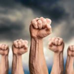 Raised fists against a cloudy sky