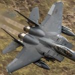 Fighter jet banking low over rugged terrain