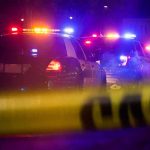 Police cars with flashing lights behind yellow caution tape at night