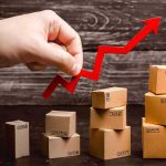 Hand holding red upward arrow over stacked cardboard boxes