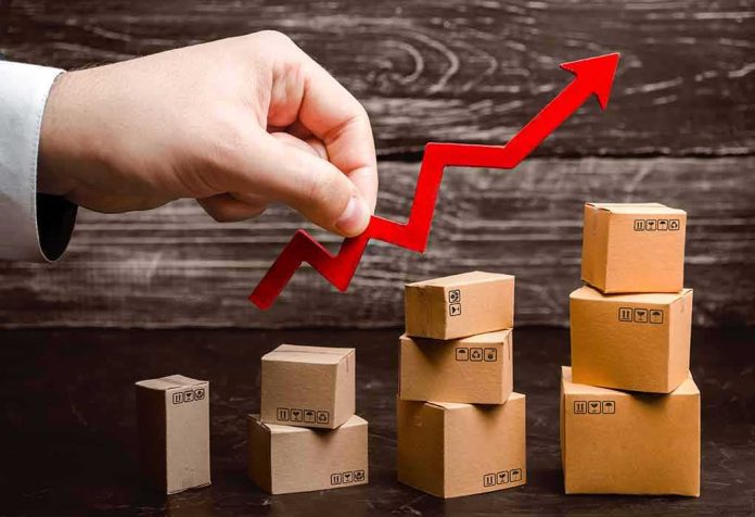 Hand holding red upward arrow over stacked cardboard boxes