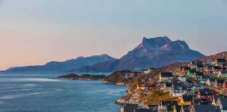 Trump Cut A Greenland Deal — Look Who The Fine Print Locks OUT Colorful coastal town with mountains and sea at sunset