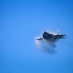 fighter jet creating vapor cone in blue sky