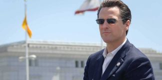 Gavin Newsom wearing sunglasses in a navy suit outdoors
