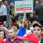 Child holding a 'Latinos for Trump' sign at a crowded rally