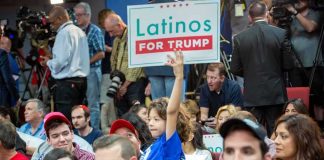 Child holding a 'Latinos for Trump' sign at a crowded rally