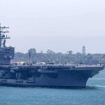 Aircraft carrier escorted by a tugboat in a harbor