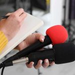 Prime Minister TOPPLES — WHY This Matters to U.S. Journalist holding two microphones while writing in a notebook