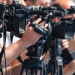 Cartoon RAID Raises CHILLING Questions television cameras on tripods at a media event