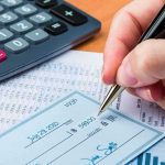 Hand writing a check beside a calculator and financial documents