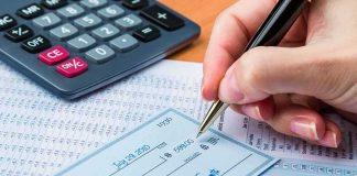 Hand writing a check beside a calculator and financial documents